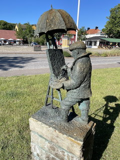 Bronze statue of two people sitting under an umbrella in a town park with buildings behind