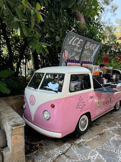 Pink vintage van with an ice cream bar parked outdoors among lush tropical plants