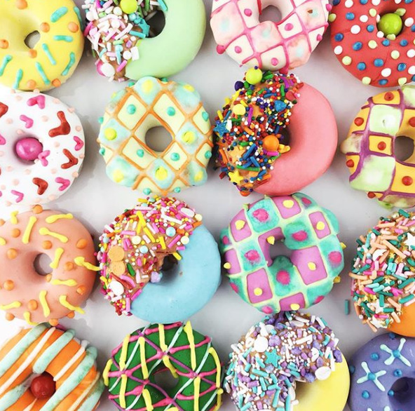 Assortment of colorful decorated donuts with various toppings and icing patterns on white surface