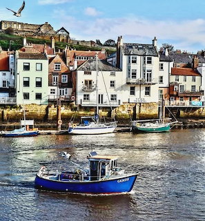 Boats on the water in Whitby harbour with houses lining the waterfront behind