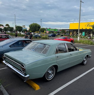 Mint green classic Ford Falcon sedan parked in a shopping center parking lot under cloudy skies