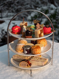Three-tier afternoon tea stand with sandwiches, scones, and holiday desserts on white plates