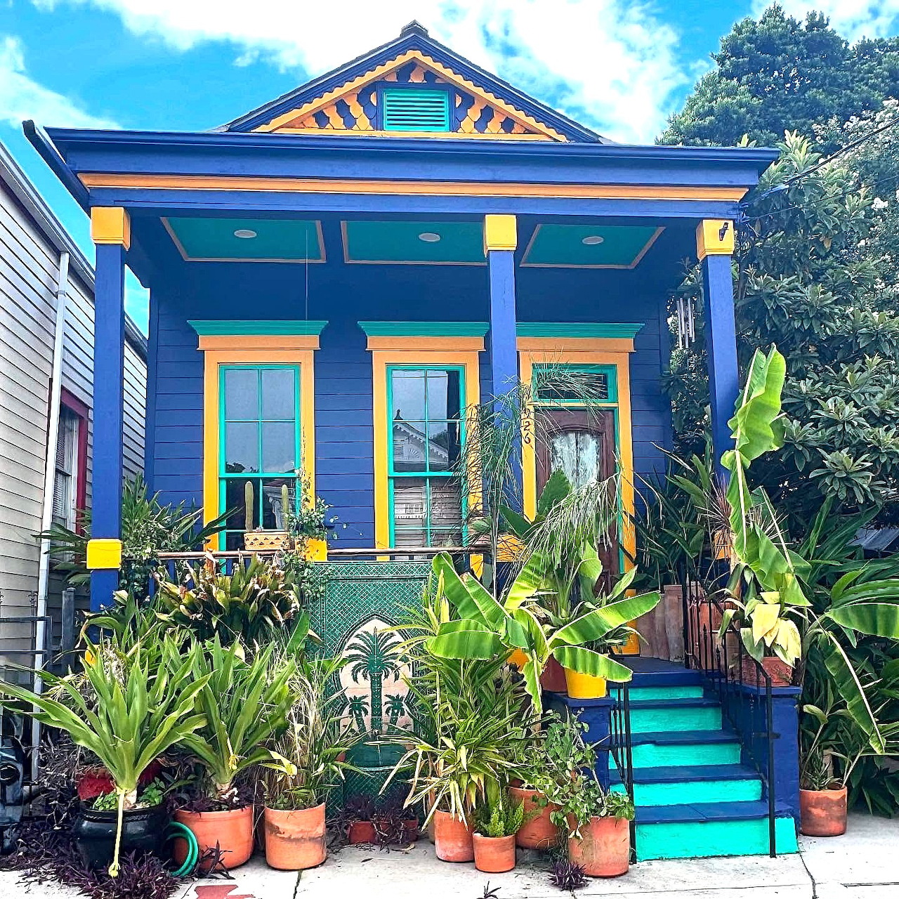 Colorful blue and orange painted Victorian house with palm trees and tropical plants on front porch