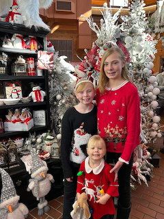 Three people in Christmas sweaters standing by decorated white trees