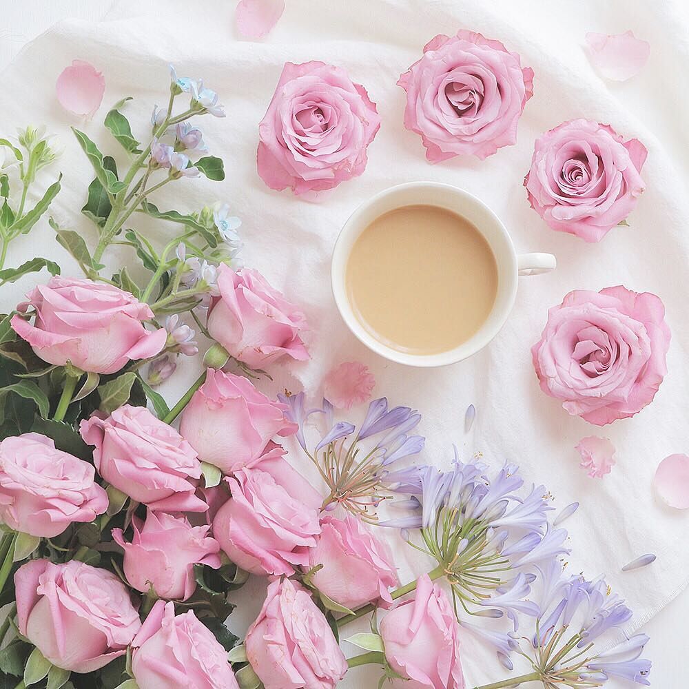 Cup of coffee surrounded by pink roses and purple flowers on white background