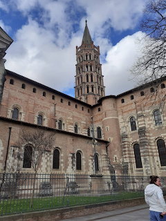 Romanesque basilica with tall octagonal brick bell tower and arched facade under cloudy blue sky