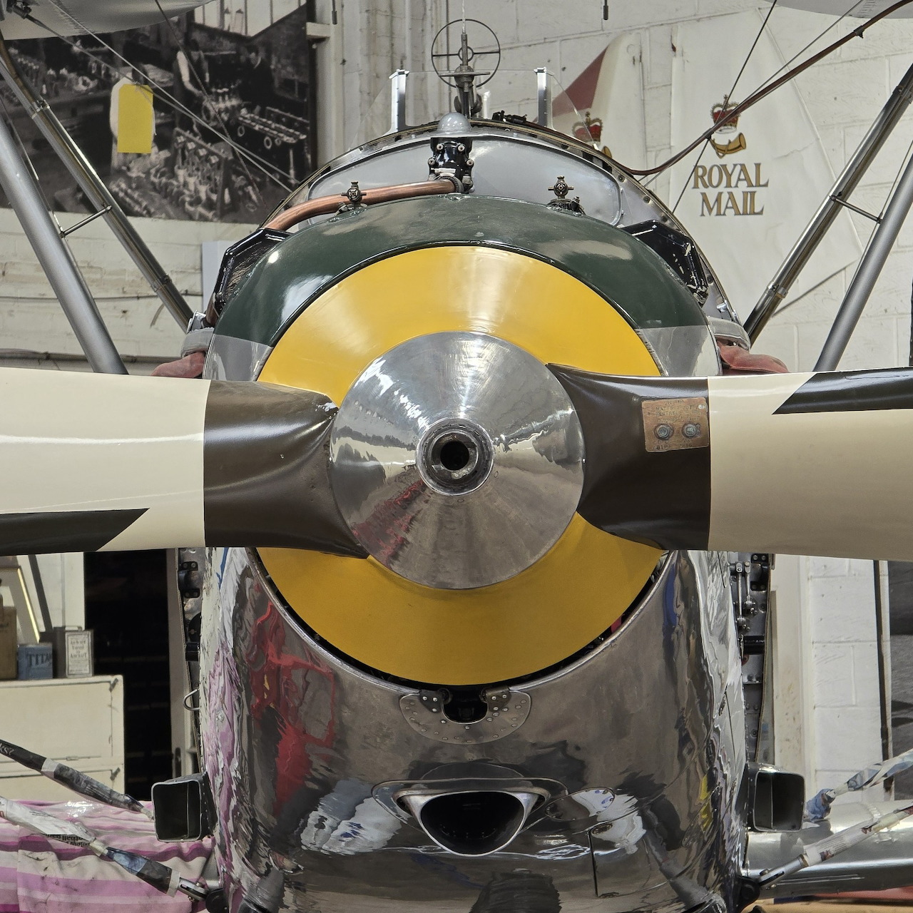 Close-up front view of vintage biplane propeller with yellow and silver engine cowling in hangar workshop