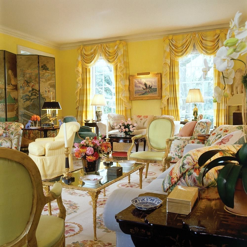 Victorian living room with yellow walls, floral sofas, ornate curtains, and antique furniture