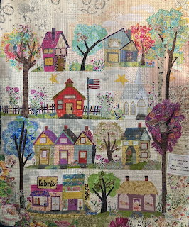 Colorful quilt artwork showing rows of small town houses with trees and flowers in a folk art style