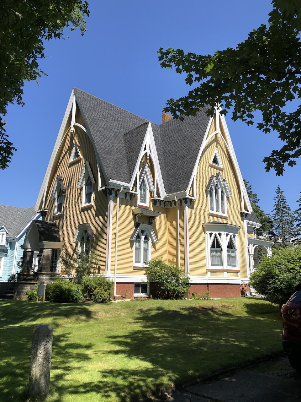 Yellow Victorian Gothic house with ornate white trim and steep gables on sunny lawn