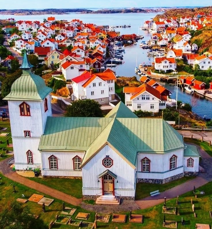 White wooden church with green roof surrounded by colorful coastal village houses near a bay