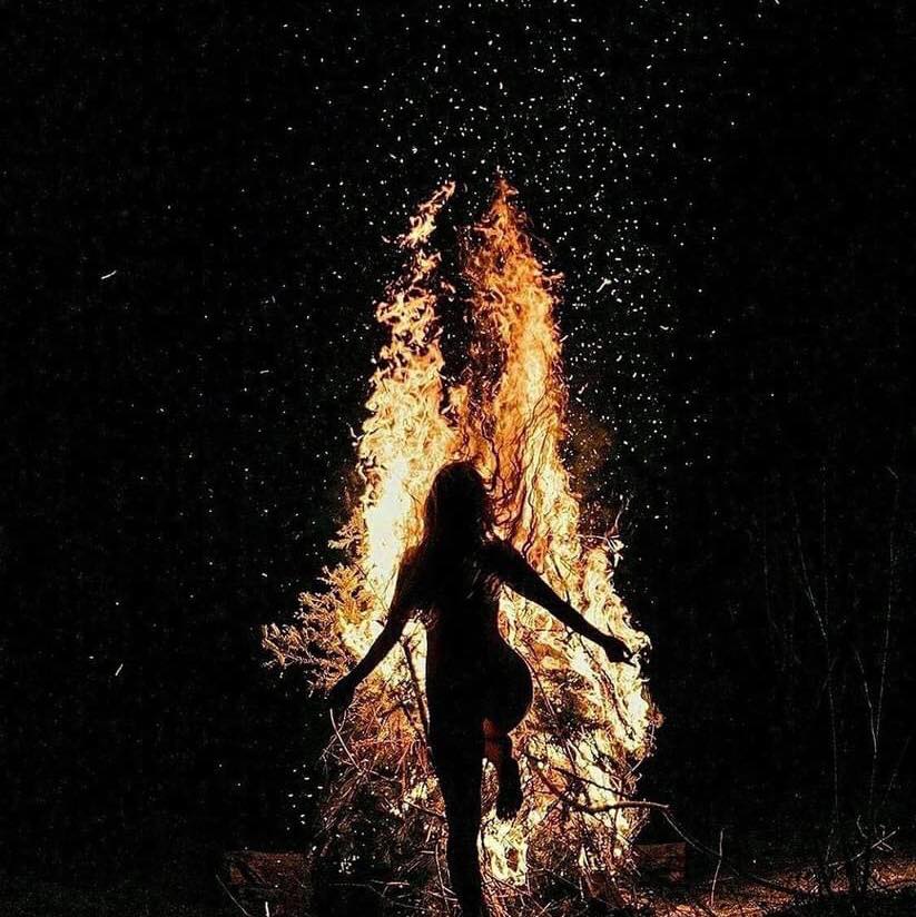 Silhouette of a woman in front of a tall bonfire at night with sparks flying