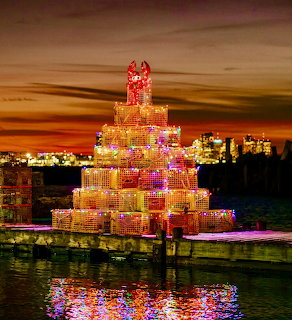 Illuminated lobster trap Christmas tree on a dock at sunset with water reflections and distant city lights