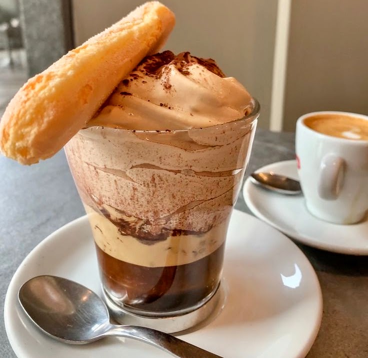 Tiramisu dessert in glass with wafer cookie and espresso cup on white plate