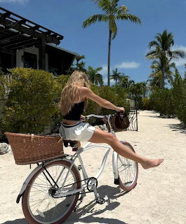 Woman in black outfit riding bicycle on sandy tropical path with palm trees