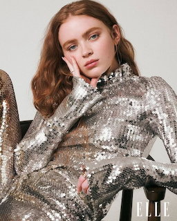 Red-haired young woman in a silver sequin turtleneck dress posing with hand near face