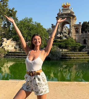 Woman with arms up posing in front of ornate fountain in park
