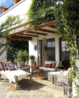 Covered outdoor patio with wicker seating, colorful cushions, poted plants, and climbing greenery