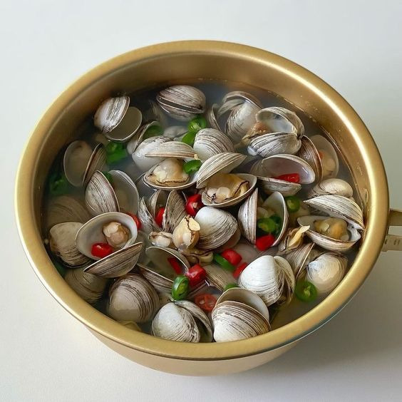 Overhead view of clam soup in golden bowl with red chilies and green herbs in clear broth