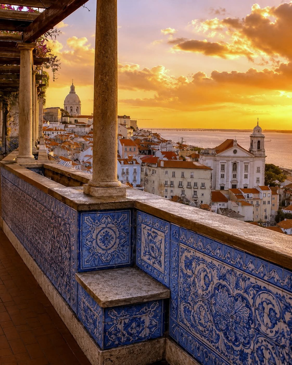 Lisbon Santa Luzia viewpoint at sunset with blue azulejo tile walls, stone columns, and cityscape beyond