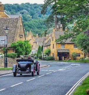 Vintage car on a street in Broadway village, Cotswolds, with traditional stone cottages and rolling green hills