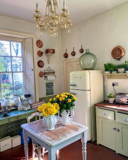 Cozy vintage kitchen with chandelier, fresh yellow flowers on table, white fridge, and green cabinetry