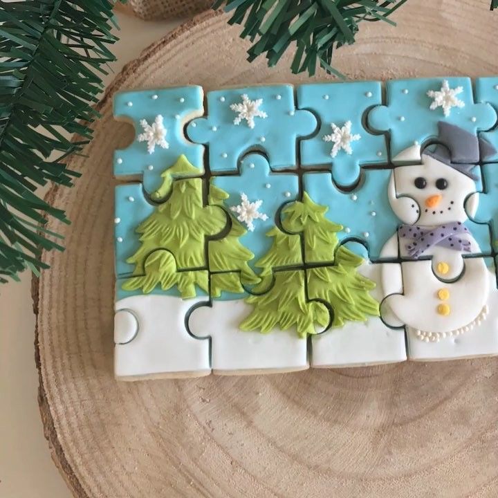 Jigsaw puzzle-shaped cookie decorated with snowman, Christmas trees, and snowflakes on blue and white icing
