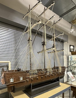 Detailed wooden model of a three-masted sailing ship with rigging on a workshop table