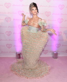 Woman in ornate beaded pastel dress with puffed sleeves against pink heart backdrop