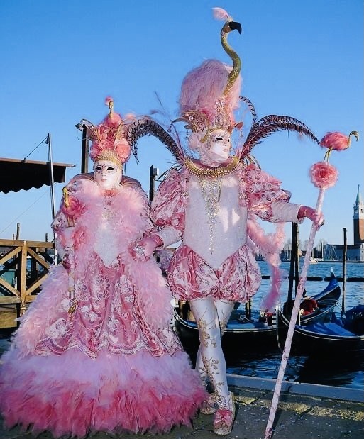 Two people in ornate pink flamingo costumes with elaborate masks and feathered headdresses at Venice Carnival waterfront