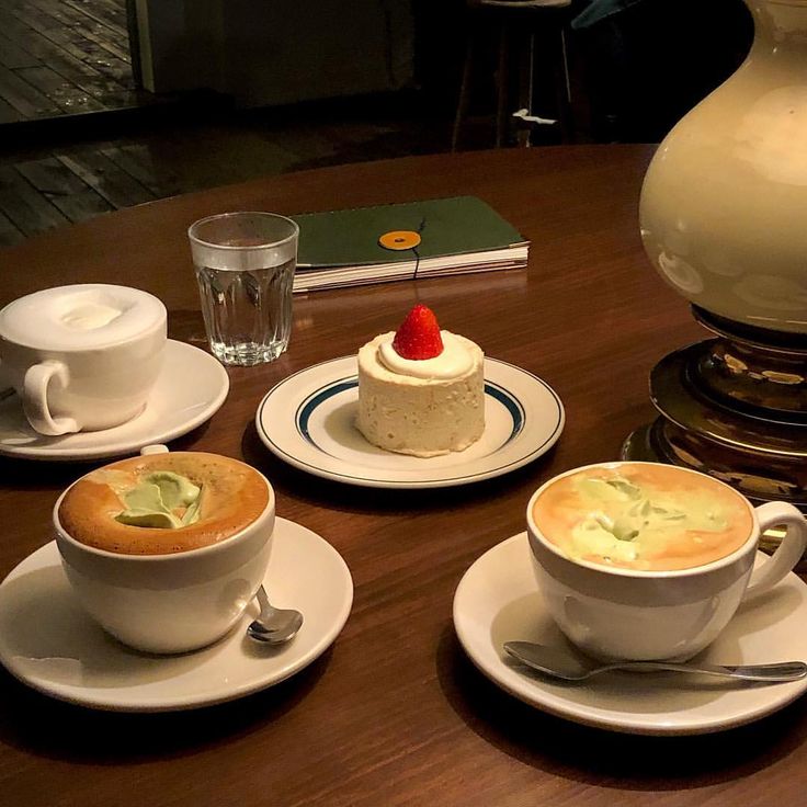 Three coffee drinks, water, and a small strawberry cake on a wooden cafe table