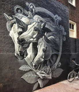 Monochrome street art mural of a horse with roses on a brick wall, bicycle parked at base