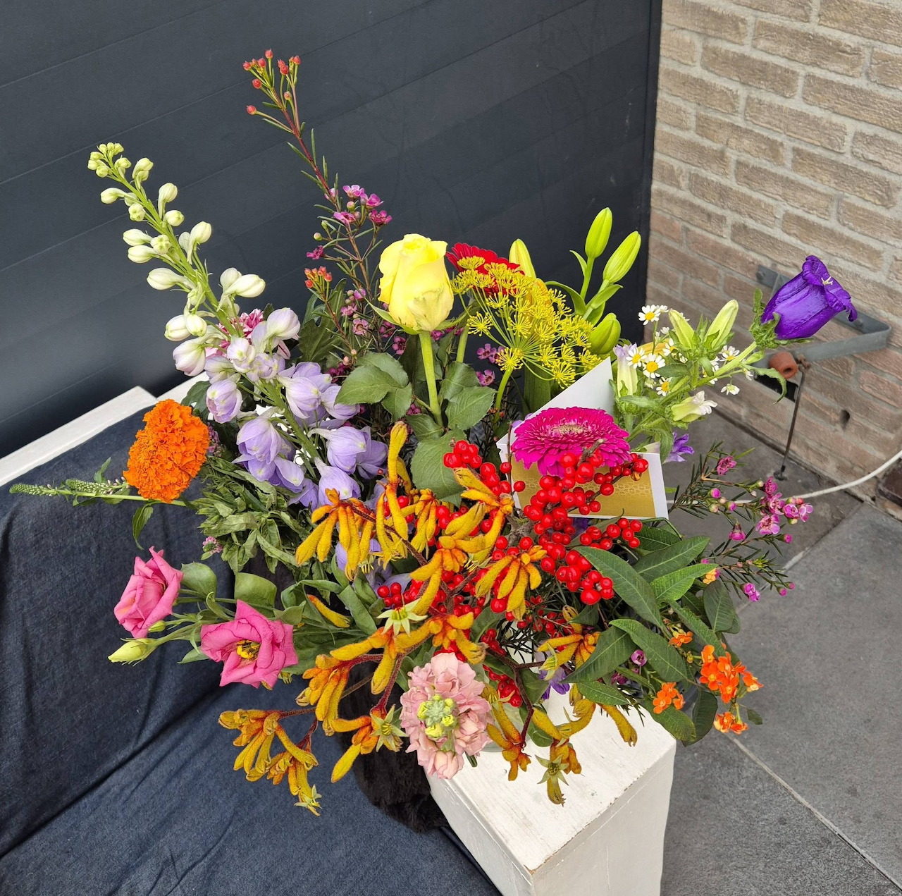 Colorful mixed flower bouquet in a white planter outdoors by a wall