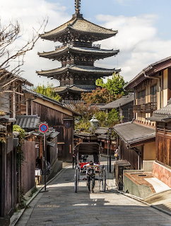 Traditional Kyoto street with wooden buildings leading to a five-story pagoda with a rickshaw on the road