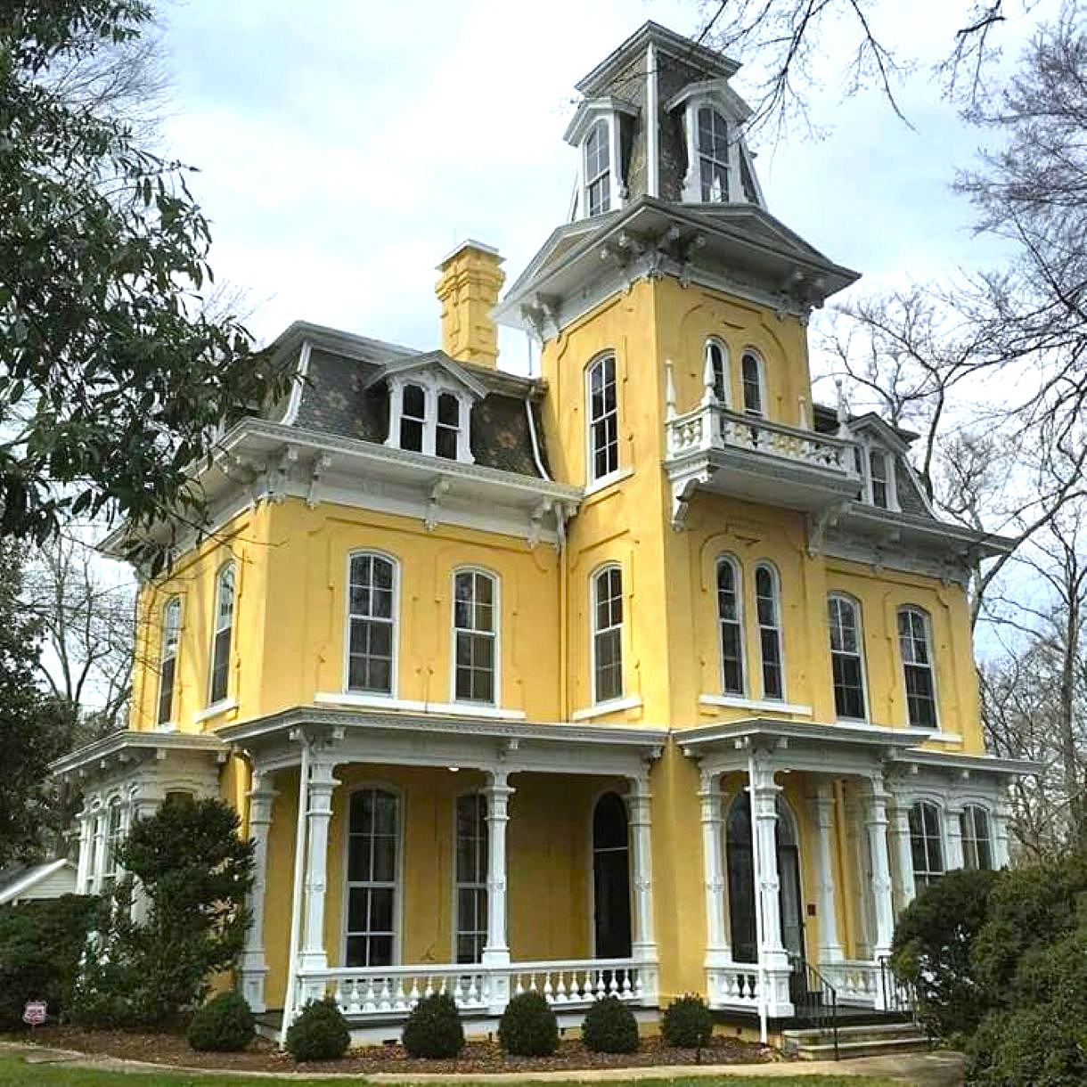 Yellow Victorian house with white trim, wraparound porch, and tower