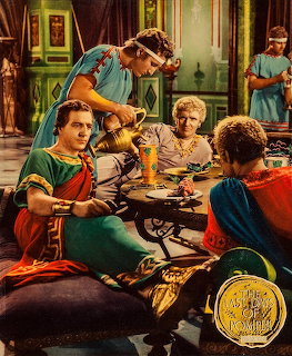 Roman banquet scene from classic film with people in colorful togas dining at a table in decorated interior