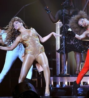 Beyoncé in a gold leotard dancing on stage with backup dancers during a live concert