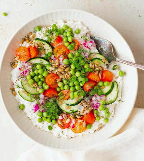 White bowl of cottage cheese salad with peas, cucumbers, tomatoes, seeds, and fresh herbs from above
