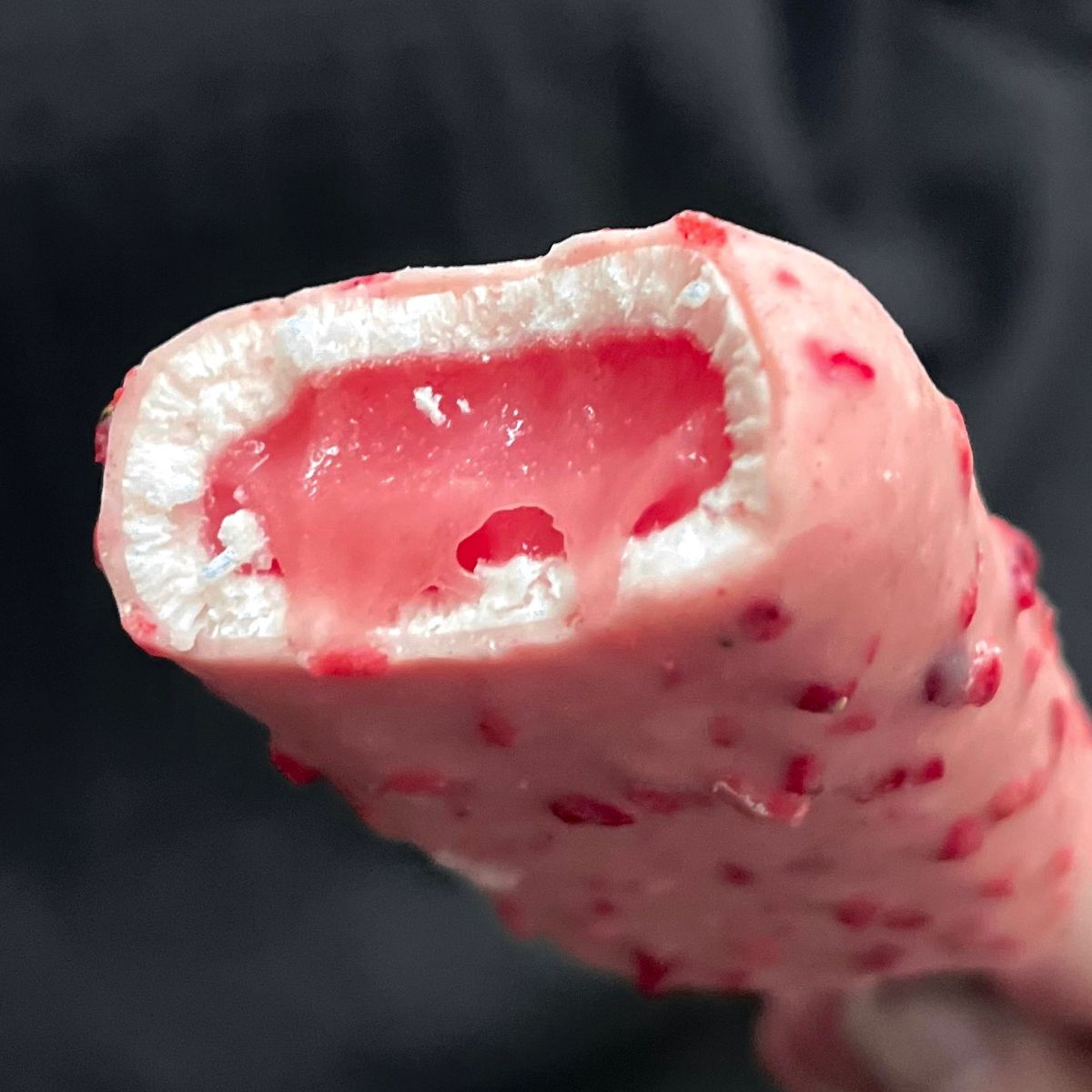 Close-up of a bitten pink ice cream bar with creamy center on a stick