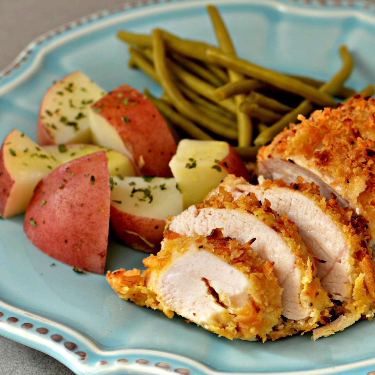 Sliced breaded chicken breast with roasted potatoes and green beans on a blue plate