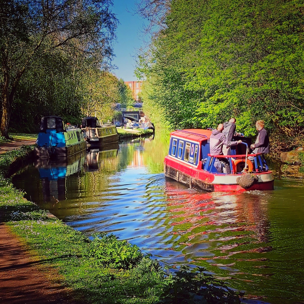 Colorful narrowboats on a calm canal surrounded by trees with reflections in the water