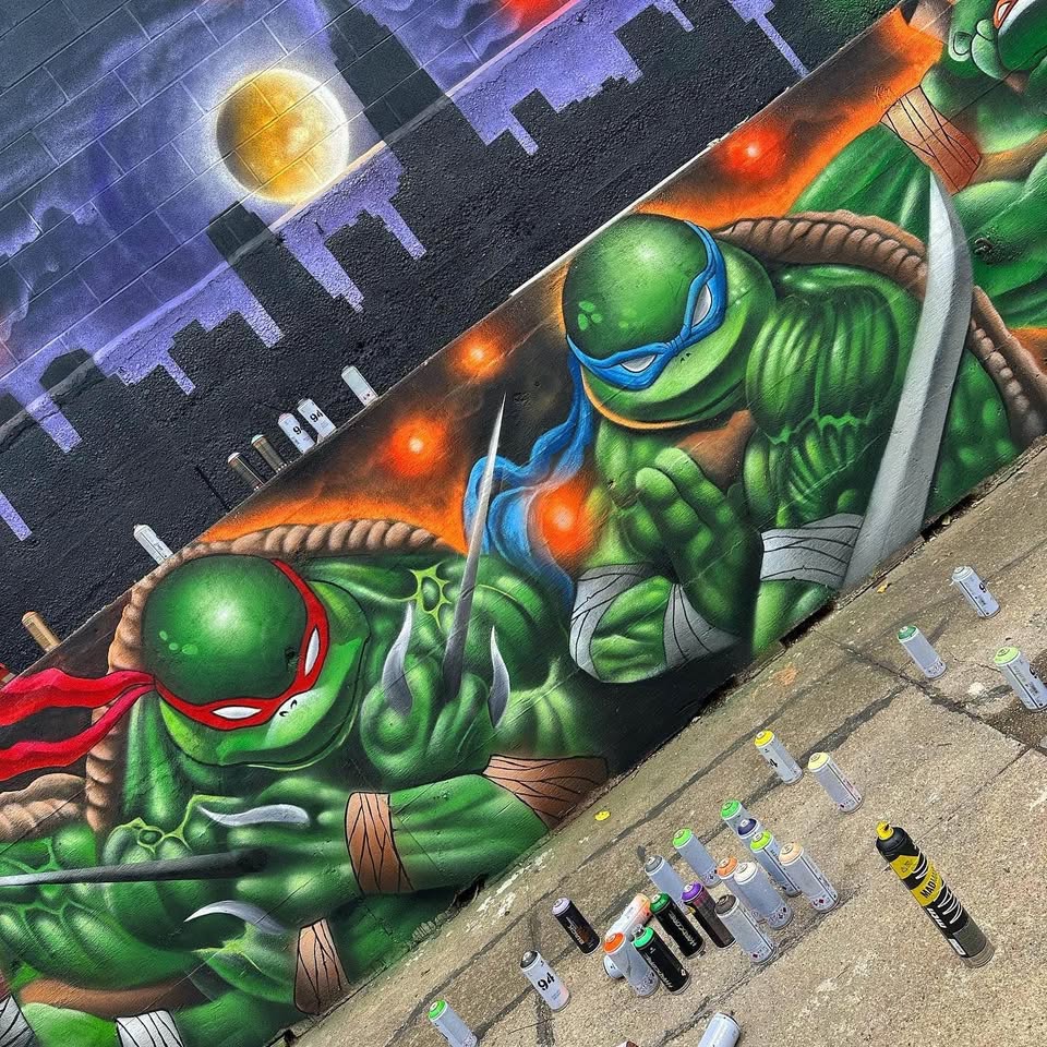 Colorful street mural showing two Ninja Turtles with weapons against a nighttime cityscape with full moon