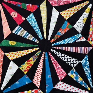 Colorful geometric patchwork quilt pattern arranged in a radial starburst on a black background