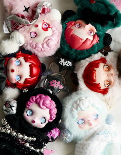 Top-down view of six stylized collectible toy figures with colorful hair and fluffy costumes