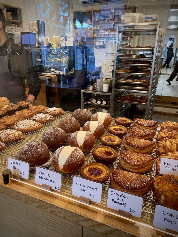 Bakery counter display with assorted pastries including bagels, tarts, and rolls with handwritten labels