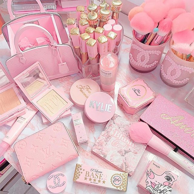 Pink cosmetics and makeup accessories arranged in a flat lay with brushes, perfume, powders, and a handbag