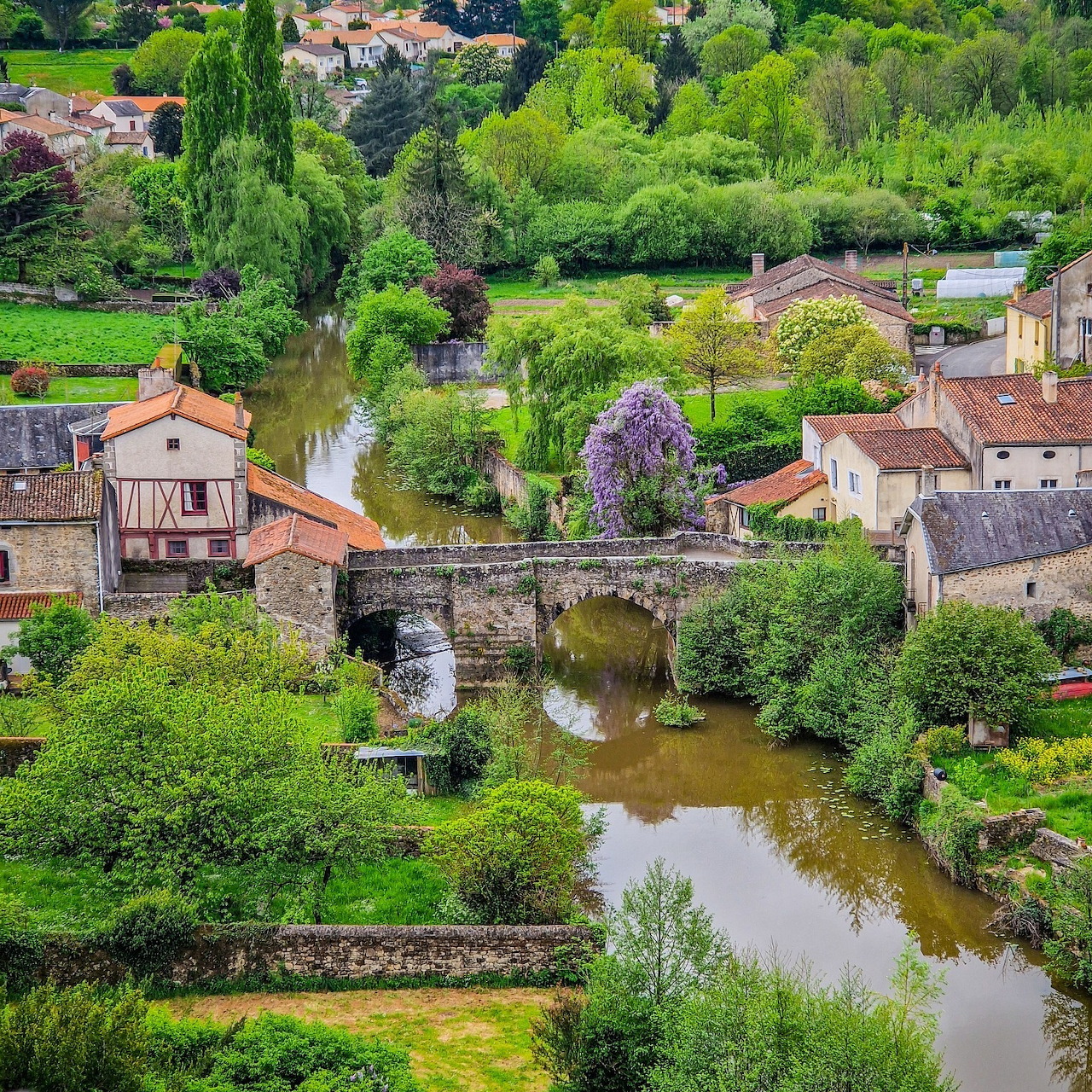 Aerial view of a French village with stone bridge crossing a river surrounded by greenery