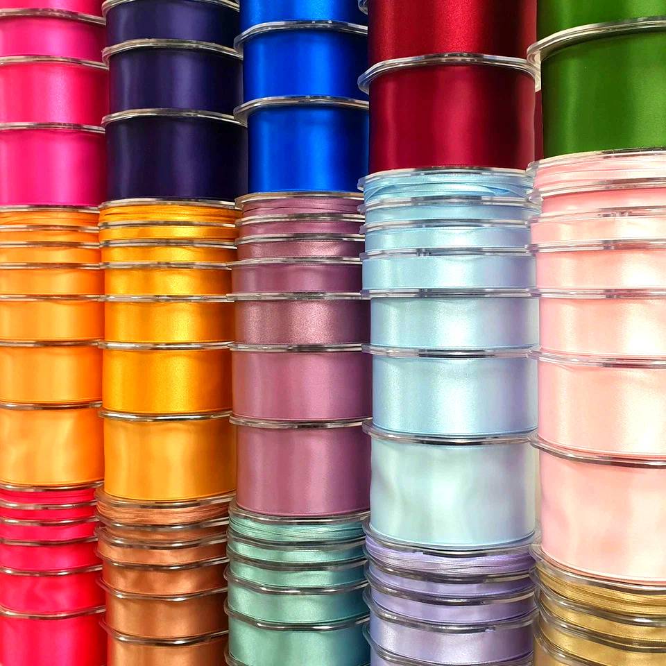 Stacks of colorful satin ribbon spools in many vibrant colors arranged closely together