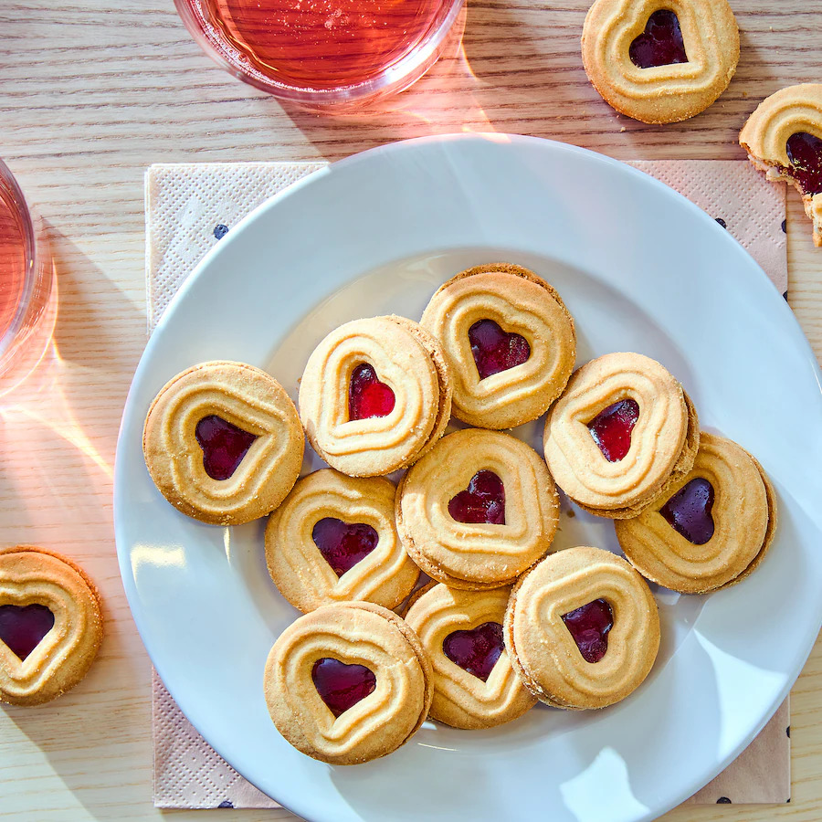 White plate full of heart-shaped shortbread cookies with red jam centers on a table