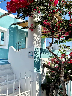 White Greek house with pink bougainvillea tree, white gate, turquoise walls, and stone steps